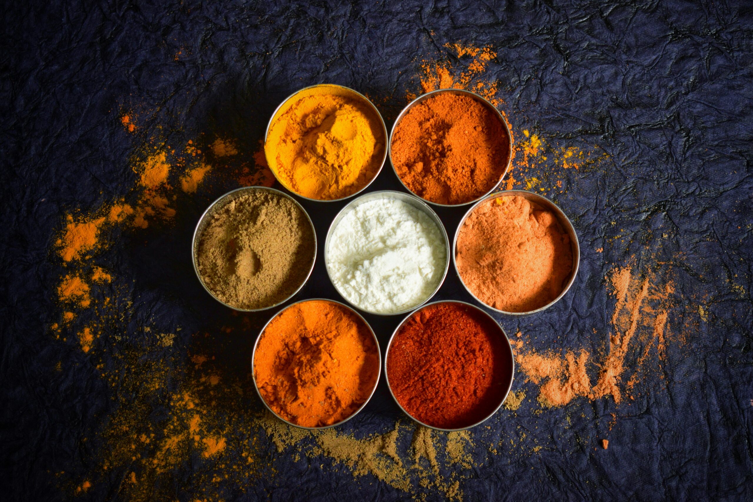 Colorful Indian spices in bowls on a textured dark background for culinary concepts.