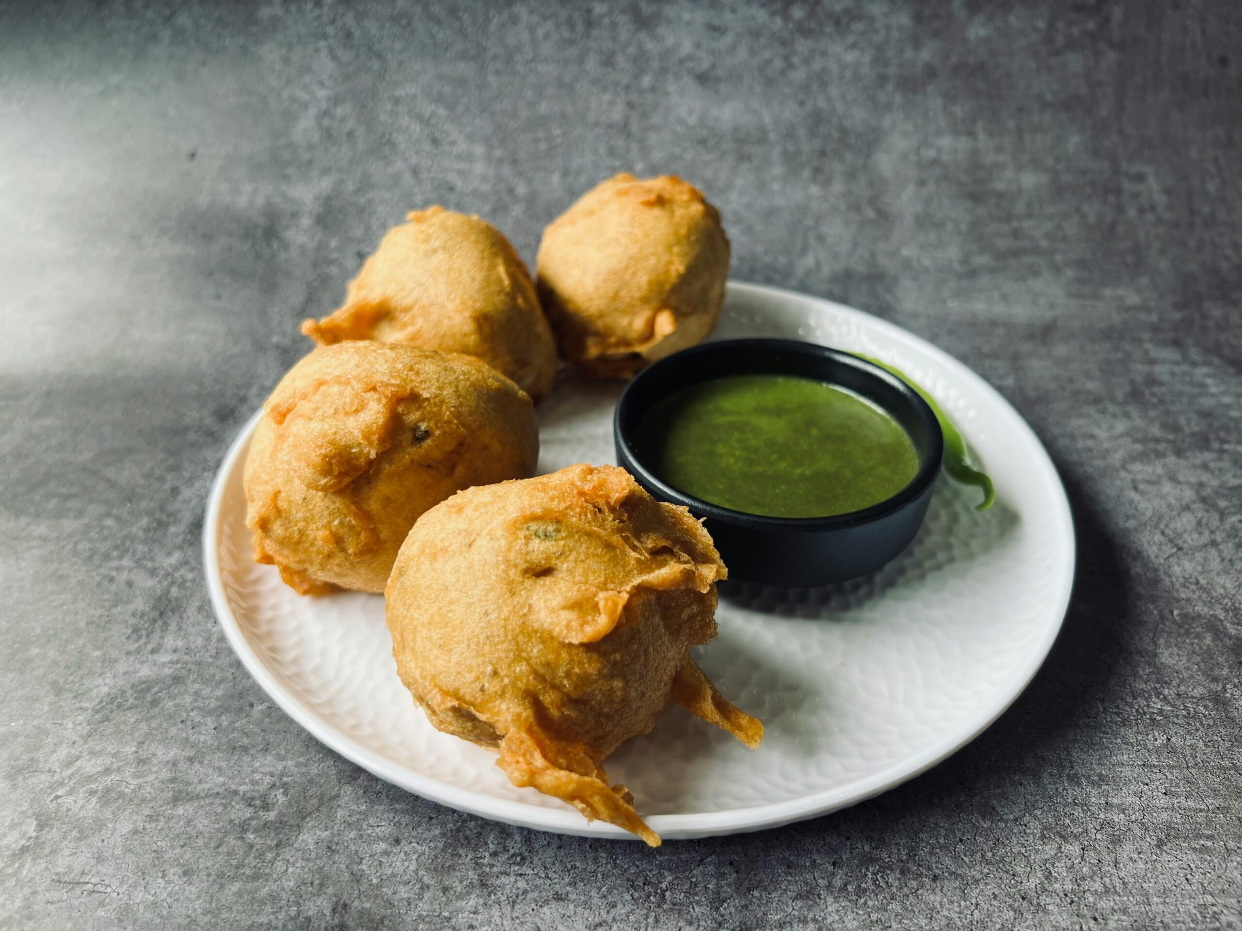 Savor the taste of crispy Indian batata vada served with flavorful green chutney on a plate.